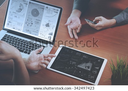 top view of two colleagues discussing data with new modern computer laptop and pro digital tablet with digital business strategy layer effect on wooden desk as concept