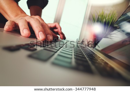 Close up of business man hand working on laptop computer with green plant on wooden desk as concept