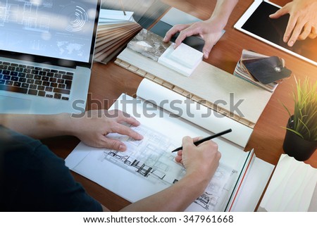 top view of two colleagues interior designers discussing data with blank screen new modern computer laptop and pro digital tablet with sample material on wooden desk as concept