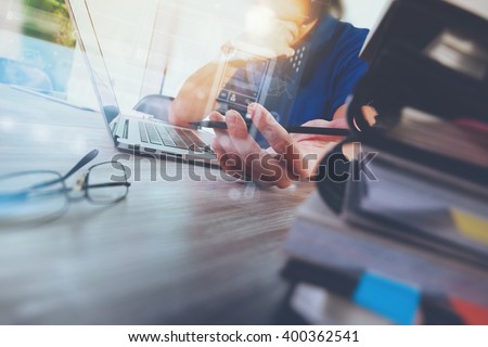 designer hand working with digital tablet and laptop computer and book stack and eye glass on wooden desk as concept