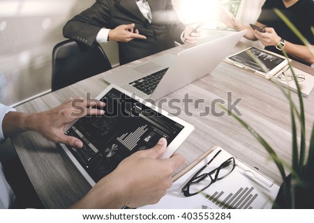 business documents on office table with smart phone and laptop computer and graph business with social network diagram and three colleagues discussing data in the background