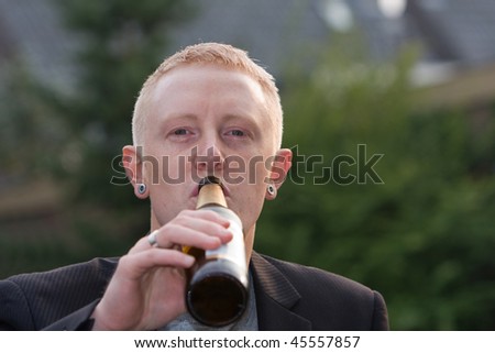A young men is drinking beer outside.