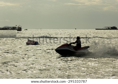 Silhouette of a man ride Jet Ski at Pattaya with banana boat background in summer