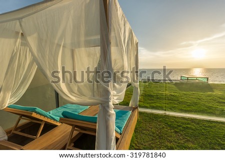 Luxury Spa Wood framed White Curtains Canopy Daybeds (Lounge chairs) Beach Tent on Grass Terrace near island Beach under Golden Sky Sunset in sea horizon in Summer in Resort at Pattaya, Thailand.