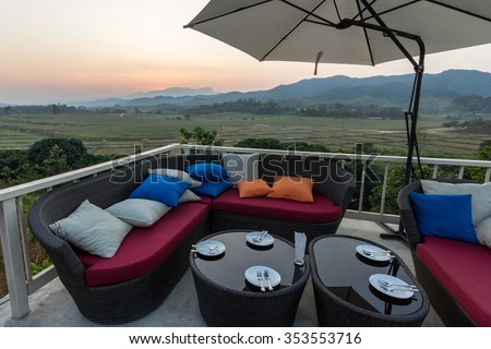 Colorful Outdoor Sofa Chair Dinner Table under Umbrella Lounge Bar Cafe Restaurant Terrace in Luxury Hotel Resort Spa with mountains view background at Dusk Evening Summer Sunset, Chiang Rai, Thailand