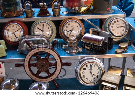 PARIS - JANUARY 13: Old clocks and boat steering wheel for sale at Boulevard de l\'Hopital flea market on January 13, 2013 in Paris, France. This flea market serves the professional antique dealers.