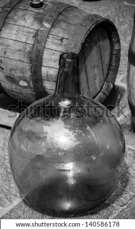 Empty round  wine bottle and wine barrel at background.  Black and white.