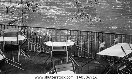Tables and chairs with rain drops. Riverside cafe after closure in Provence. Black and white.