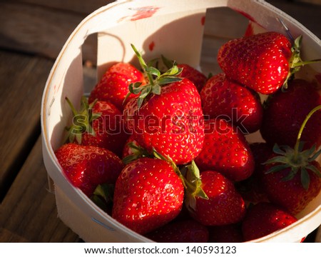 Strawberries in a basket on wooden background. Long evening shadows.