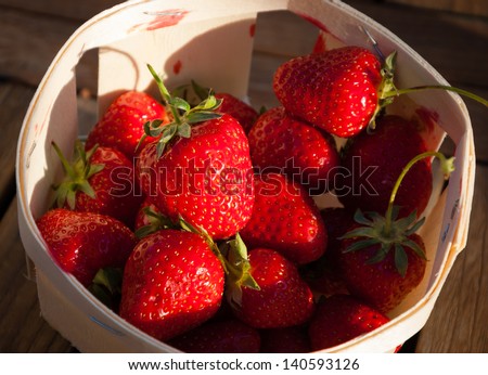 Strawberries in a basket on wooden background. Long evening shadows.