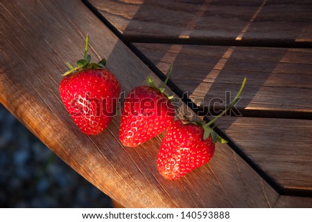 Three fresh strawberries on wooden background. Long evening shadows.