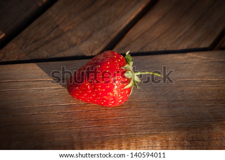 Single strawberries berry on wooden background. Long evening shadows.