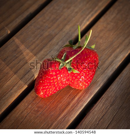 Two fresh strawberries on wooden background. Long evening shadows.