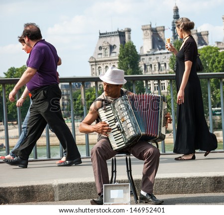 PARIS - JULY 6: Unidentified senior musician play accordion on the bridge near  Hotel de Ville and the tourists passing by on July 6, 2013 in Paris, France. Dozens buskers perform on streets of Paris.