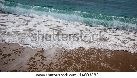 Sea wave with white foam rolling on the beach sand.