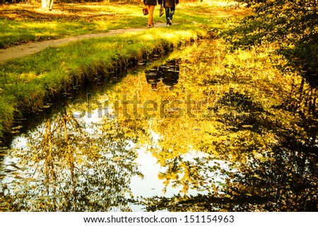 Golden autumn in park. Reflection of trees and walking couple in water. Shadowed angles.