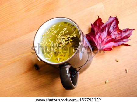 Cup of fennel tea with seeds on wooden background with maroon maple leaf decoration.