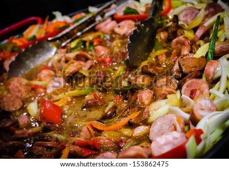 Hot stewed sausage and meat  with vegetables  in big pan at street market.  Closeup. Raising steam. Christmas market in Paris.