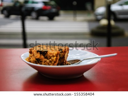 Break idea. Slice of carrot pie with walnuts on the red table  in the cafe with the city view. Pedestrian crossing bringing to the cake. Selective focus.
