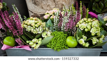 Flowers arrangement with green apples and pink bow in metal box at the entry to the flower shop.