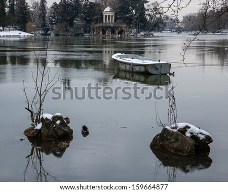 Snow covered boat in the lake and Love Temple at backgrounds.  Lake Daumesnil (Vincennes forest, Paris, France).