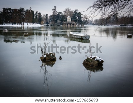 Snow covered boat in the lake and Love Temple at backgrounds.  Lake Daumesnil (Vincennes forest, Paris, France). Shadowed angles.