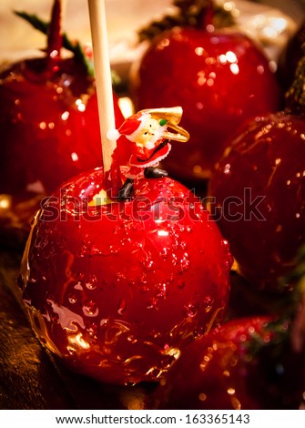 Red toffee love apple decorated with Santa Claus playing saxophone. Christmas market in Paris. Shadowed angles.
