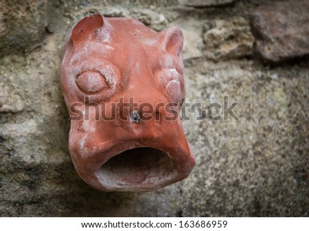 Old ceramic downspout in shape of beast head against stone wall. Closeup. Shadowed angles.