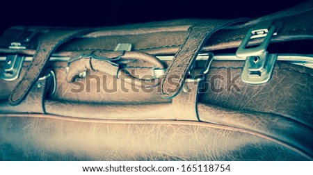 Vintage leather briefcase with straps and brass buckles on black background. Travel concept. Toned image. Selective focus on the right side of the image.