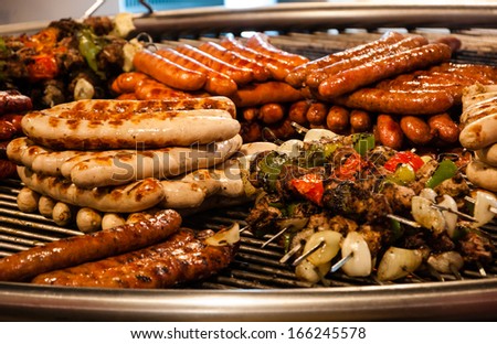 Assortment Of Grilled Sausages And Kebabs On Big Round Grill At Christmas Market In Paris. Selective Focus On The Sausages On Left Side.