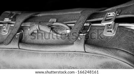 Vintage leather briefcase with straps and brass buckles on black background. Travel concept. Black and white. Selective focus on the right side of the image.