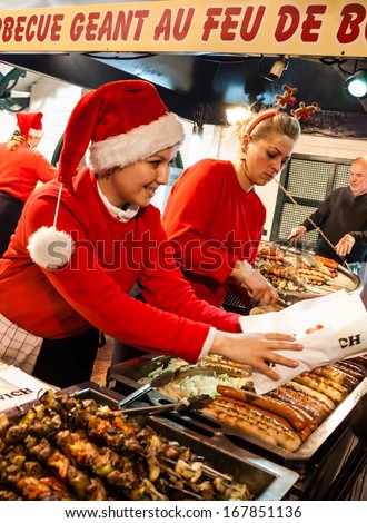 PARIS - NOV 30: Unidentified women in Santa Claus hats cook and sell hotdogs and barbecue at Christmas market  on November 30, 2013 in Paris, France.