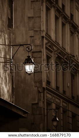 Lantern on the building wall. Paris, France. Sepia. Aged photo. Sunlight is highlighting the lantern attached to the wall and the rest of the street is in the shadow. Retro style postcard.