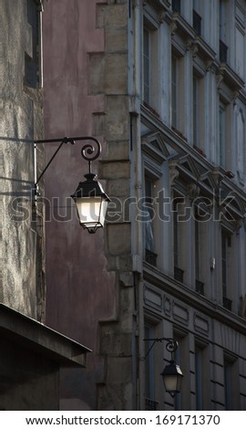 Lantern on the building wall. Paris, France. Sunlight is highlighting the lantern attached to the wall and the rest of the street is in the shadow.