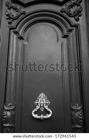 Royal style doorknocker on wooden door. Black and white.
