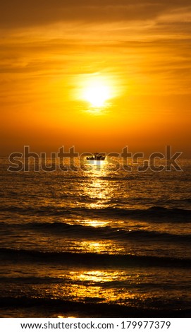 Silhouette of the fisherman or leisure boat sailing toward golden sunset with saturated sky and clouds. Beautiful seascape in the evening. Harmony with nature idea. Tranquility and freedom background.