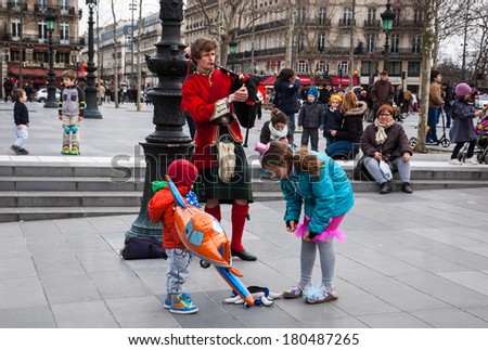 PARIS, FRANCE - MARCH 2, 2014: Young Scottish bagpiper in traditional costume plays music at  Place de la Republique before the public and the unidentified children put the money into his hat.