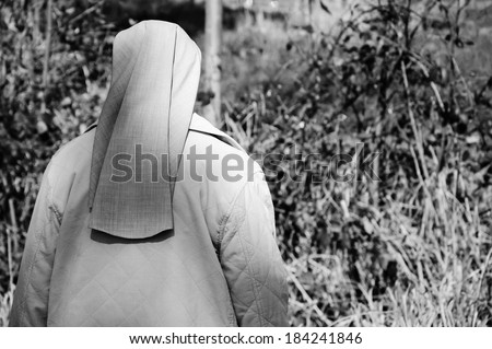A nun in grey robe in the forest. A game of light and shadow. Religion and nature. Meditation background. Harmony, God in nature idea. Aged photo. Black and white.
