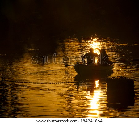 Silhouettes of  a man and woman in the boat on the lake. Sunset. Light and shadow. Romance background. Harmony with nature idea. Light and shadow.