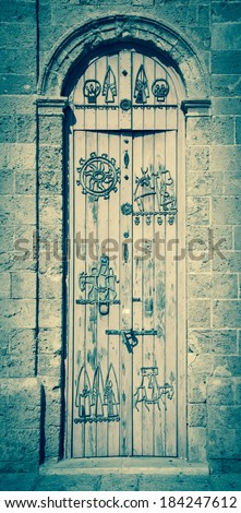 Old wooden door with iron figurative decoration (man travelling on donkey, etc). Architectural detail of Jaffa Clock Tower built in Ottoman period. Jaffa, Israel. Aged photo.