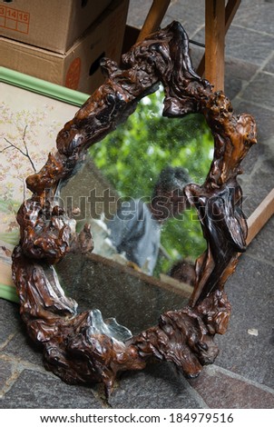 Dirty vintage mirror in curved wooden frame at flea market. Blurred reflection of two unidentified persons and tree.