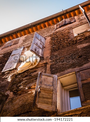 Blanket and pillow are dried, hanging out of the window of old typical house with weathered wooden shutters and rough stone wall in medieval town Castellane (Provence, France).