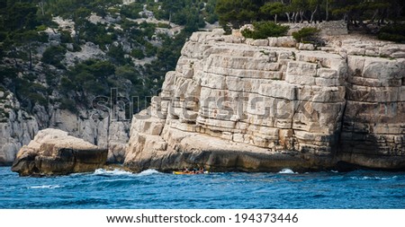 Three men row in the canoe between the rocks in the famous Calanques national park of Cassis (near Marseilles in Provence, France)