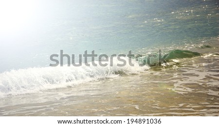 Sea wave with white foam rolling on the beach sand. Sun beams and glow.