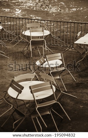 Tables and chairs with rain drops. Riverside cafe after closure in Provence. Aged photo. Sepia.