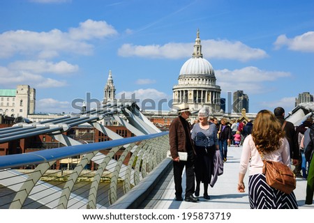 LONDON, ENGLAND, UK - MAY 3, 2014: Tourists walking across the Millennium Bridge, which was opened in 2000. St Paul\'s cathedral is seen at backgrounds.