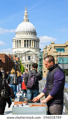 LONDON, ENGLAND, UK - MAY 3, 2014: Unidentified man prepares and sells sugared nuts to the tourists crossing the Millennium Bridge toward Saint Paul cathedral.