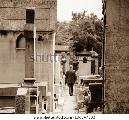Old man walking in Montparnasse Cemetery in Paris (France). Rear view. Selective focus on the cross and tomb at foreground. Aged photo.  Sepia.