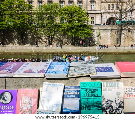 PARIS, FRANCE - APRIL 20, 2013: Bouquiniste stands over Seine river and tourist boat. Selling books on the banks of the Seine began around the 16th century.