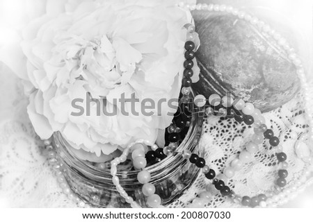 Vintage background with pink peony, jewels in glass jar and old rusty iron ball on the lace. Light glow. Aged photo. Black and white.